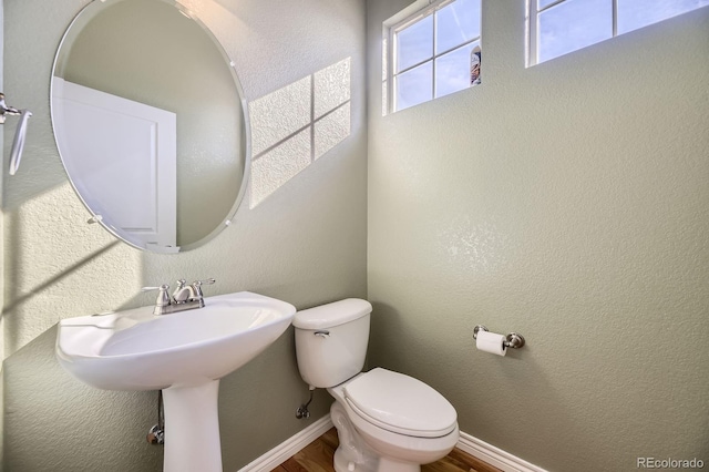 half bath with toilet, wood finished floors, baseboards, and a textured wall