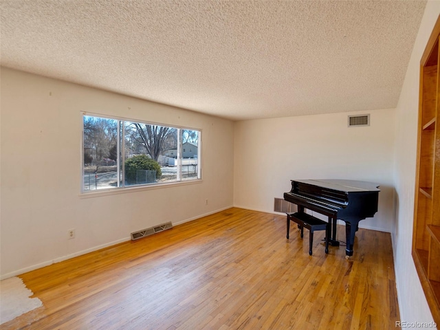 living area with a textured ceiling, visible vents, and light wood-style floors