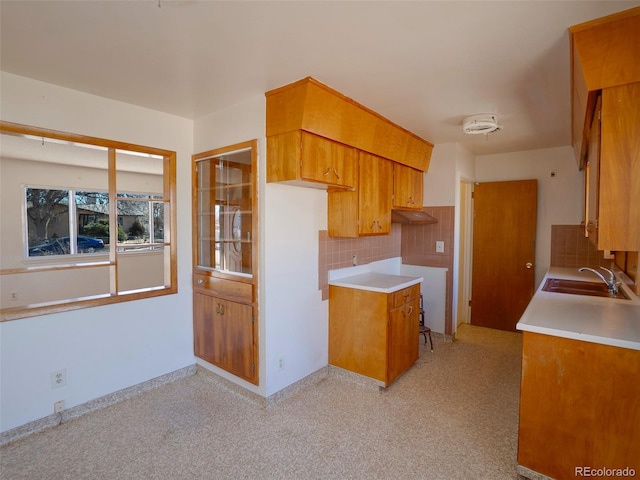 kitchen with brown cabinets, tasteful backsplash, light countertops, a sink, and under cabinet range hood