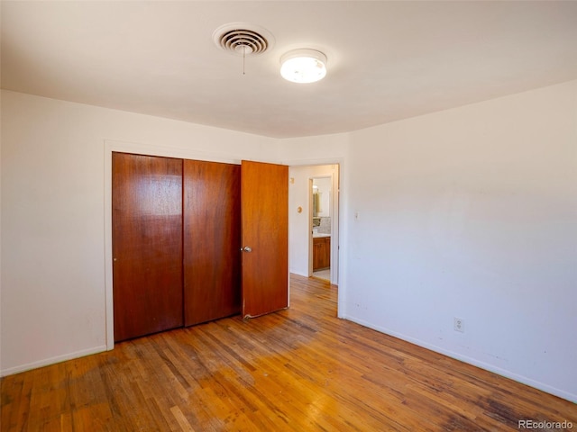 unfurnished bedroom with a closet, visible vents, baseboards, and hardwood / wood-style floors