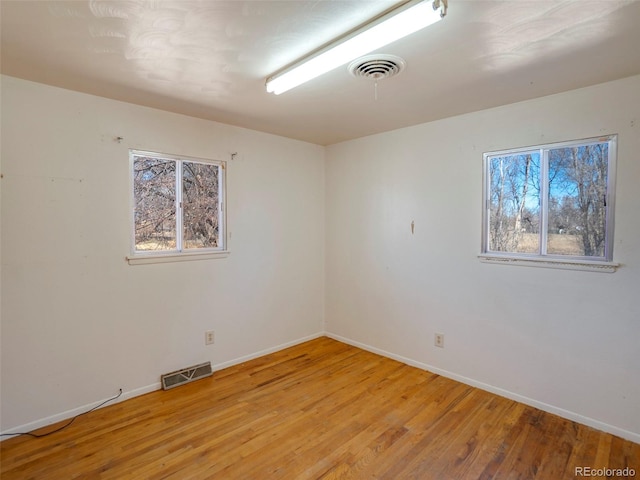 empty room with light wood finished floors, visible vents, and baseboards