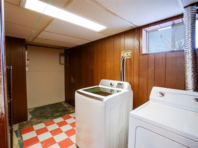 clothes washing area featuring light floors, wood walls, and independent washer and dryer