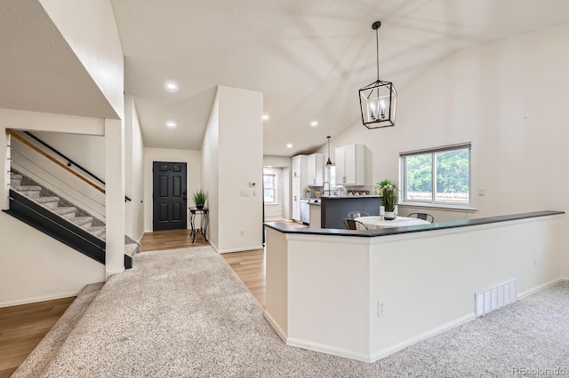 3455 Sun River Pl, Colorado Springs, CO 80920 - kitchen with white cabinetry, lofted ceiling, dark countertops, light wood-style floors, and hanging light fixtures