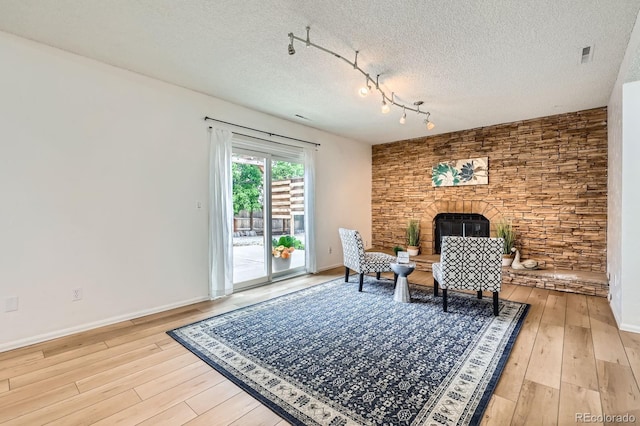 3455 Sun River Pl, Colorado Springs, CO 80920 - living area with light wood-style floors, a large fireplace, a textured ceiling, rail lighting, and baseboards