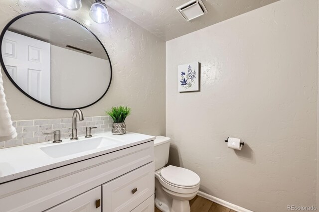 3455 Sun River Pl, Colorado Springs, CO 80920 - half bath featuring decorative backsplash, toilet, vanity, wood finished floors, and a textured wall