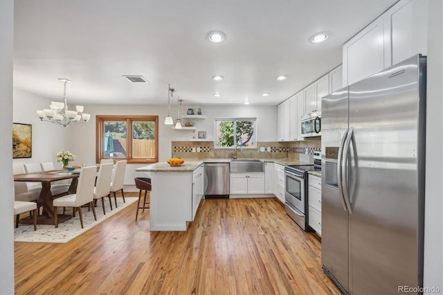 kitchen with appliances with stainless steel finishes, light hardwood / wood-style flooring, pendant lighting, and white cabinets