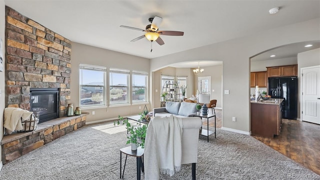 8308 Needle Drop Ct, Colorado Springs, CO 80908 - living room featuring arched walkways, a ceiling fan, dark colored carpet, a chandelier, and a stone fireplace
