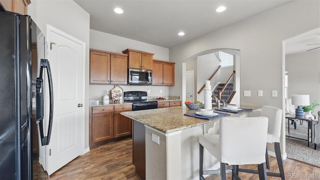8308 Needle Drop Ct, Colorado Springs, CO 80908 - kitchen with black appliances, light stone countertops, brown cabinetry, a breakfast bar, and arched walkways