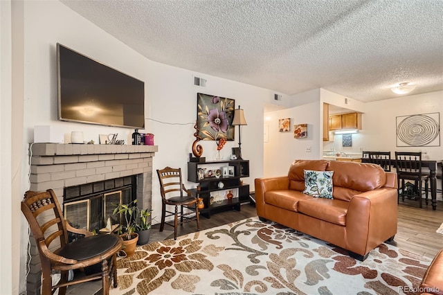 living area featuring a textured ceiling, a brick fireplace, wood finished floors, and visible vents