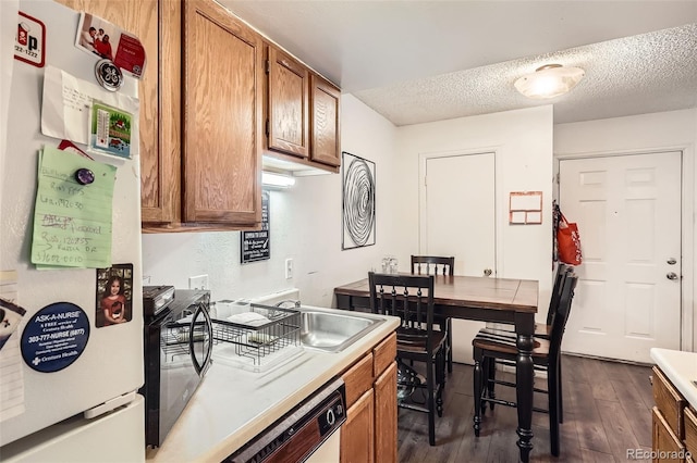 kitchen featuring a textured ceiling, white appliances, dark wood-style flooring, light countertops, and brown cabinetry