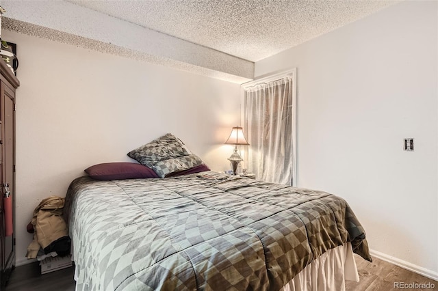 bedroom with a textured ceiling, wood finished floors, and baseboards