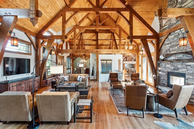 living room featuring a stone fireplace, light hardwood / wood-style flooring, wooden ceiling, a notable chandelier, and beamed ceiling