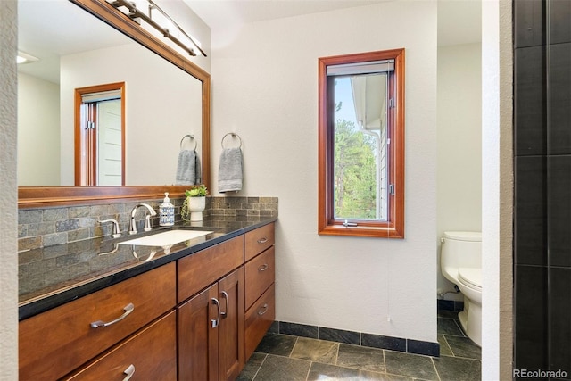 2122 Cramner Ct, Evergreen, CO 80439 - bathroom featuring vanity, toilet, baseboards, stone tile flooring, and backsplash