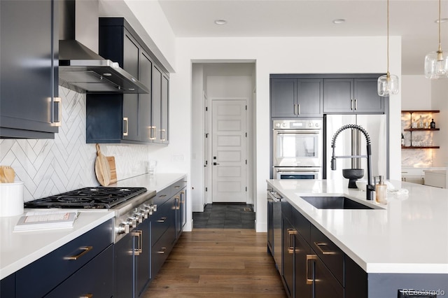 kitchen featuring stainless steel appliances, a sink, light countertops, wall chimney range hood, and backsplash