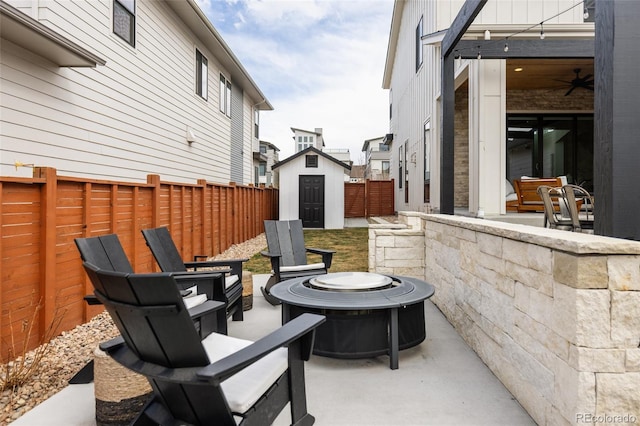 view of patio / terrace featuring a storage shed, an outdoor fire pit, a fenced backyard, and an outbuilding