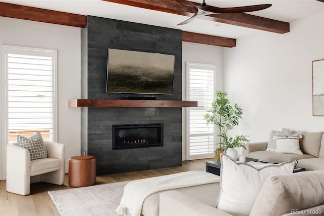 living room featuring a large fireplace, wood finished floors, beam ceiling, and a ceiling fan