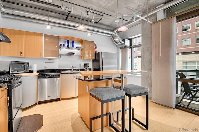 kitchen with a sink, a kitchen breakfast bar, stainless steel appliances, light wood-type flooring, and a kitchen island