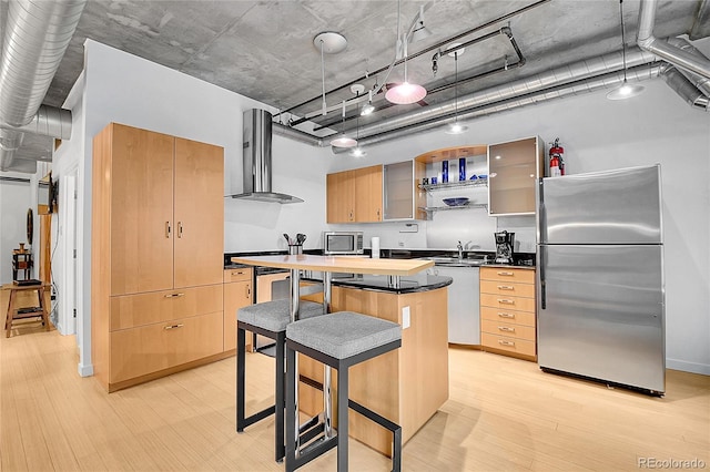 kitchen with appliances with stainless steel finishes, a sink, light wood-style floors, wall chimney exhaust hood, and a kitchen island