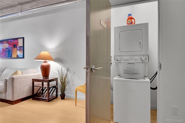 clothes washing area with laundry area, baseboards, wood finished floors, and stacked washer / dryer