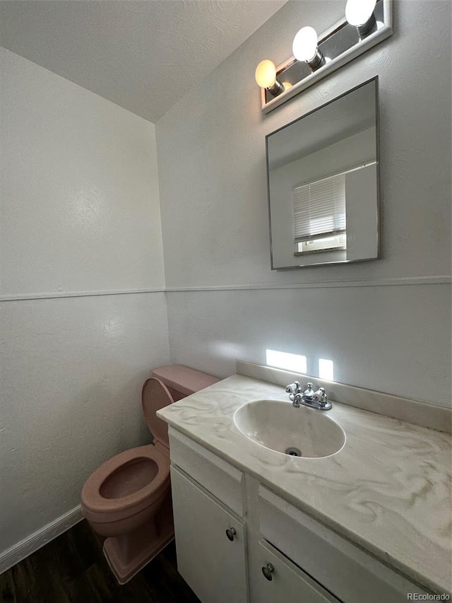 bathroom with a textured ceiling, toilet, hardwood / wood-style flooring, and vanity with extensive cabinet space