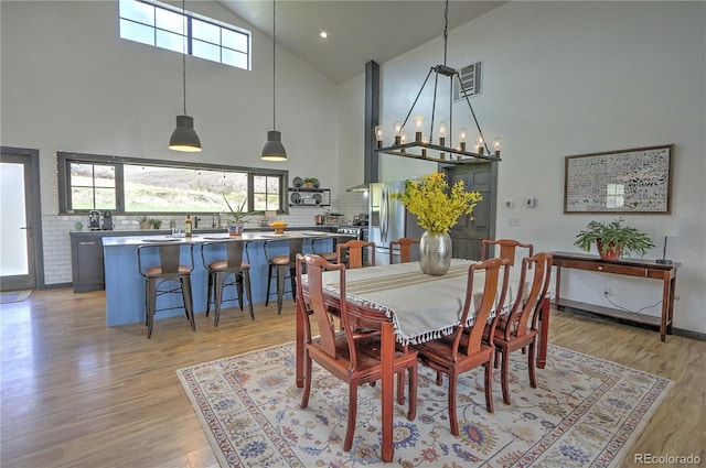 dining area featuring high vaulted ceiling, plenty of natural light, visible vents, and light wood-style flooring