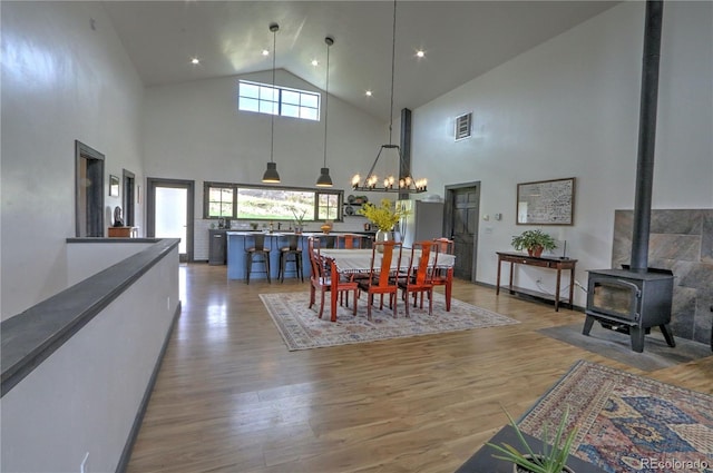 dining space featuring light wood-style floors, a wood stove, high vaulted ceiling, and an inviting chandelier