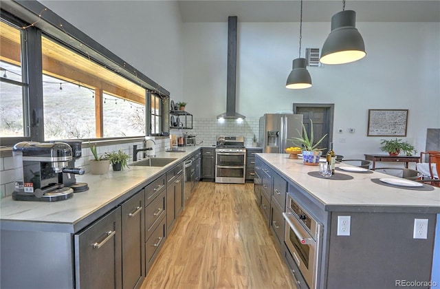 kitchen featuring a sink, a towering ceiling, light wood-style floors, decorative backsplash, and appliances with stainless steel finishes