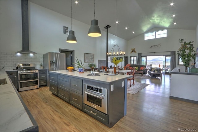 kitchen featuring visible vents, wall chimney range hood, light wood-type flooring, appliances with stainless steel finishes, and high vaulted ceiling