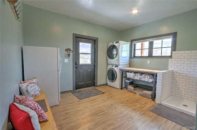 washroom featuring light wood-style flooring, stacked washing maching and dryer, and a healthy amount of sunlight