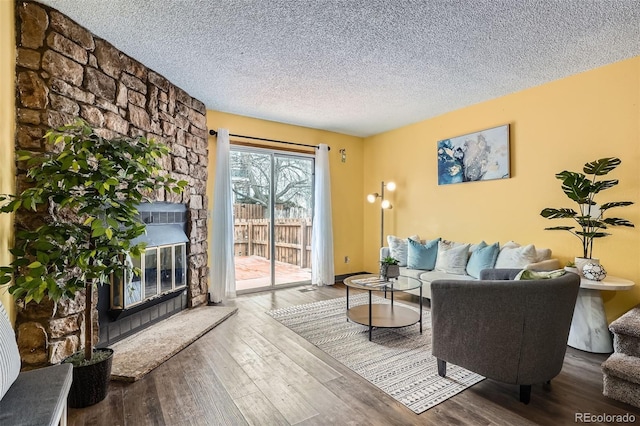 living room with a textured ceiling, a stone fireplace, and wood finished floors