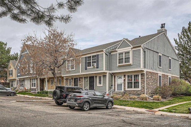 townhome / multi-family property featuring stone siding, a shingled roof, uncovered parking, and a chimney