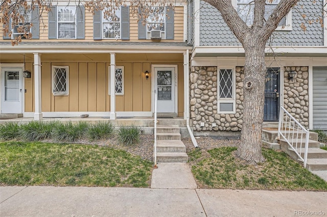 doorway to property with covered porch, board and batten siding, and stone siding