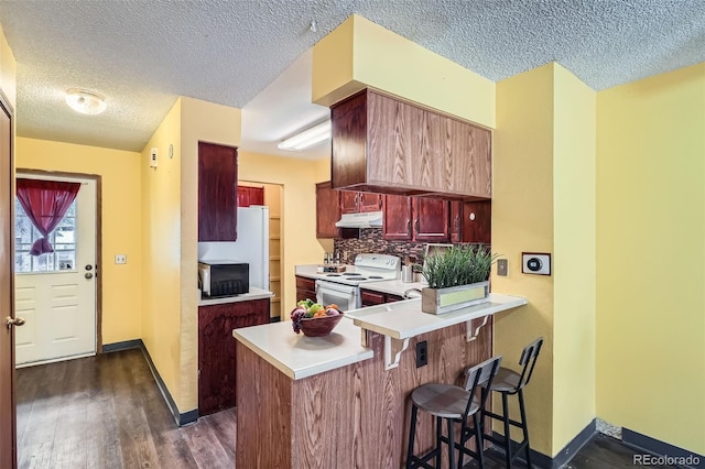 kitchen with under cabinet range hood, a textured ceiling, white appliances, and baseboards