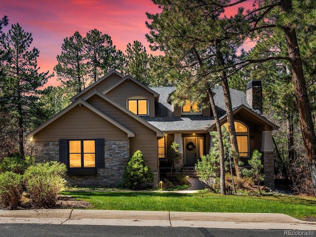 view of front of home with a chimney, stone siding, a shingled roof, and a front yard