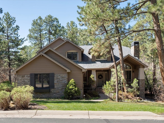 view of front of house featuring stone siding, a chimney, roof with shingles, and a front yard