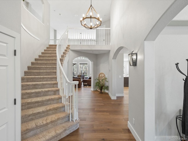 entryway featuring arched walkways, stairway, wood finished floors, a chandelier, and a high ceiling