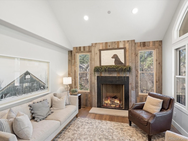living room featuring vaulted ceiling, a warm lit fireplace, wood finished floors, healthy amount of natural light, and recessed lighting