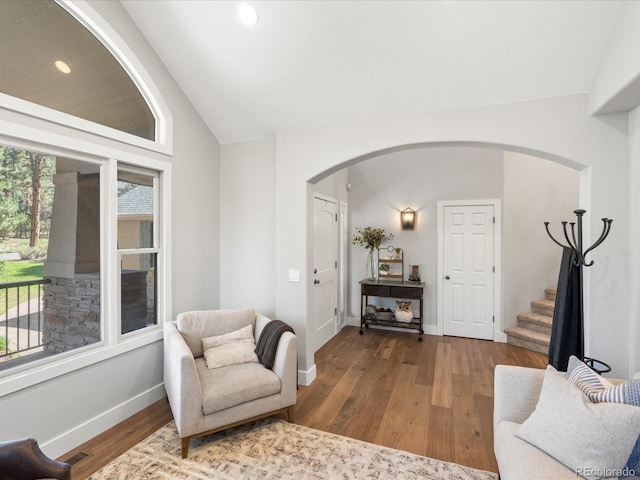 living area featuring arched walkways, lofted ceiling, wood finished floors, stairway, and baseboards