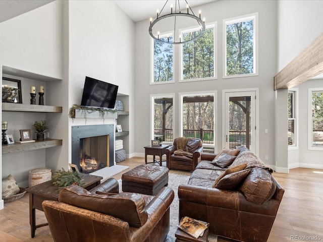 living area featuring a high ceiling, wood finished floors, a warm lit fireplace, a chandelier, and baseboards