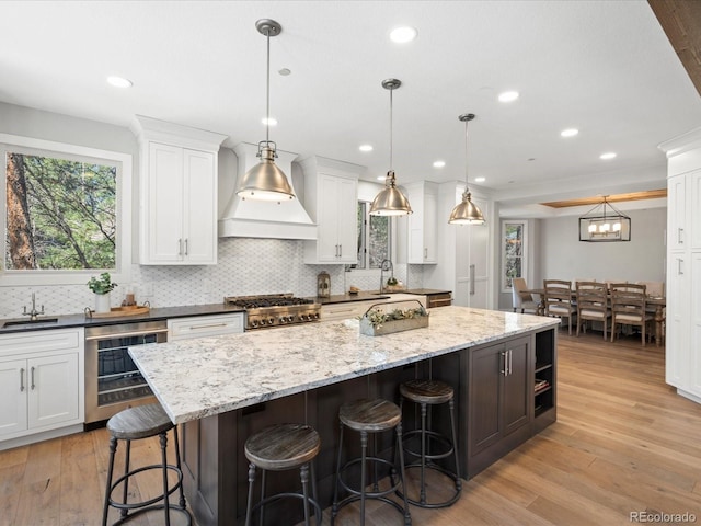 kitchen featuring beverage cooler, a kitchen island, premium range hood, backsplash, and a sink