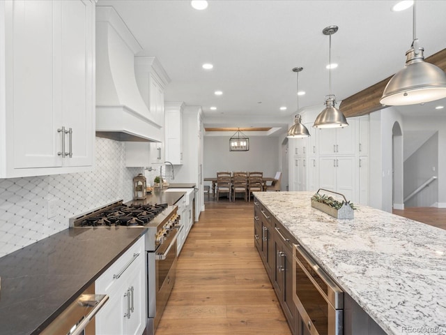 kitchen featuring stainless steel appliances, custom exhaust hood, dark stone counters, white cabinets, and recessed lighting