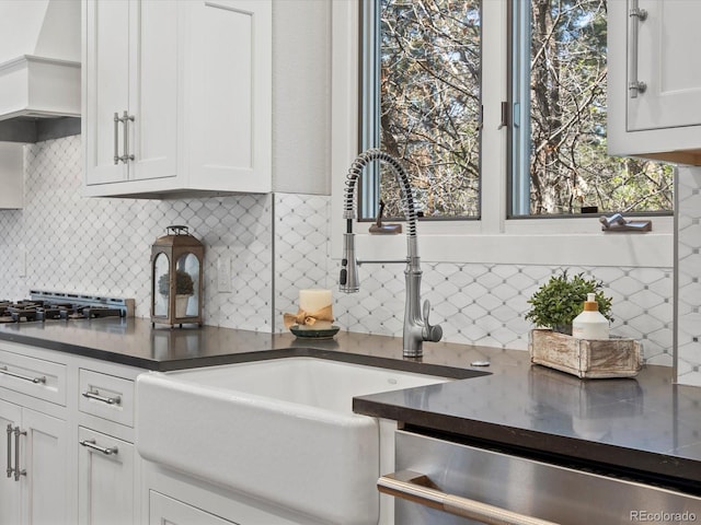 kitchen featuring a sink, dishwasher, white cabinets, backsplash, and dark countertops