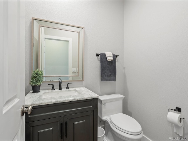 bathroom featuring toilet, vanity, and a textured wall
