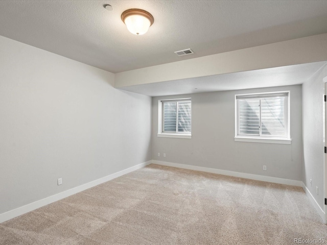 spare room with light colored carpet, healthy amount of natural light, baseboards, and a textured ceiling