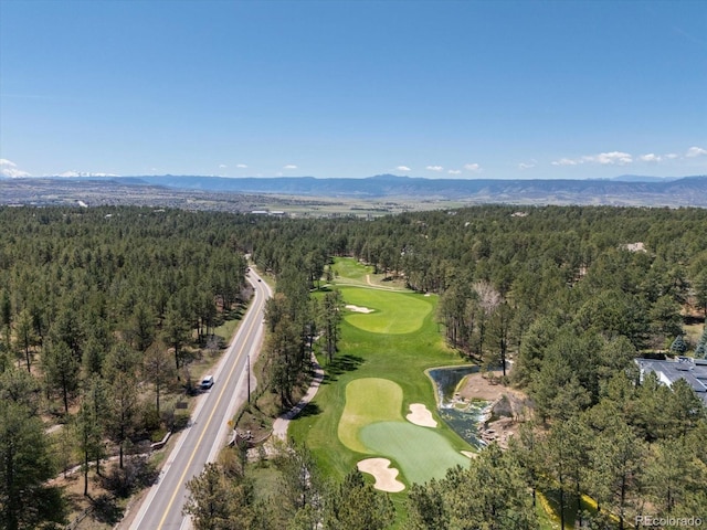 view of property location featuring a heavily wooded area, a golf club, and a mountainous background