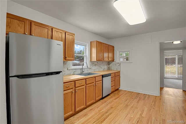 kitchen with stainless steel appliances, a sink, light countertops, backsplash, and light wood finished floors