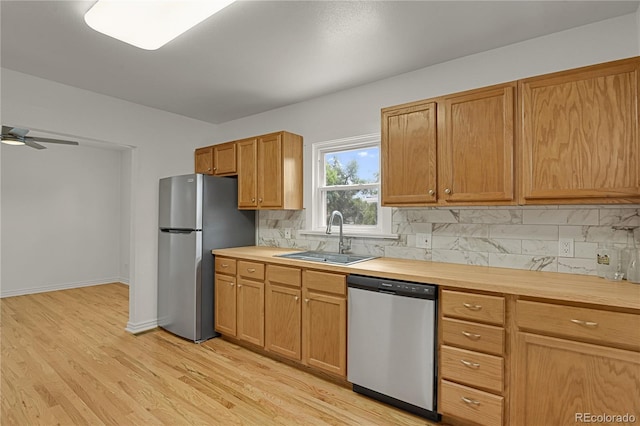 kitchen with light wood finished floors, tasteful backsplash, ceiling fan, stainless steel appliances, and a sink