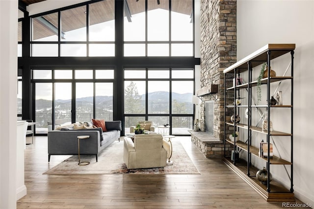 living room with a stone fireplace, hardwood / wood-style floors, a mountain view, a wall of windows, and high vaulted ceiling