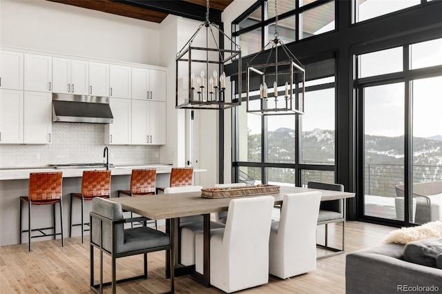 dining area with a high ceiling, beamed ceiling, an inviting chandelier, light wood-type flooring, and a mountain view