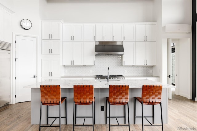 kitchen featuring light stone counters, white cabinets, a breakfast bar, and an island with sink